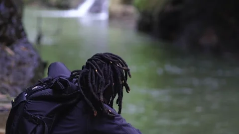 Young Man With Dreadlocks Focusing on to a Small Waterfall Stock Footage 207751972