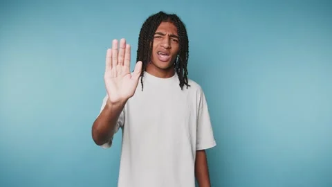 Young man with dreadlocks making a stop gesture against blue background. Stock Footage 315162844