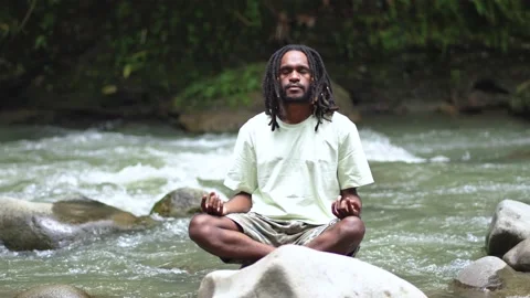 A Young Man With Dreadlocks Meditating Above a Rock Stock Footage 207397507