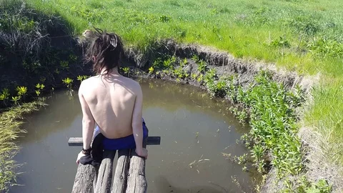 Young man with dreadlocks sits on the shore of the lake and enjoys nature Stock Footage
