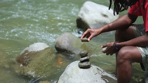 A Young Man With Dreadlocks Try to Stabilize Stack of Stones Stock Footage 207659119