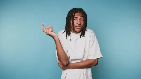 Young man with dreadlocks in a white t-shirt shrugging against a blue backg.. Stock Footage 315162840