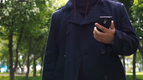 A young man dressed in a black coat talking on a mobile phone in the park. Vídeo Stock 91553985
