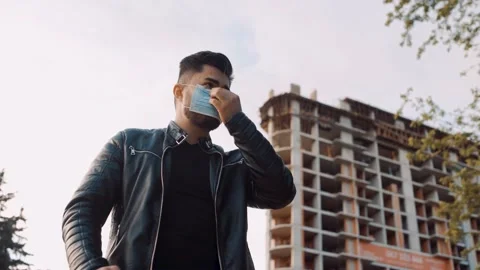 A young man dressed in a black leather jacket puts on a protective surgical mask Stock Footage 131661046