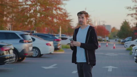 Young man dressed casually, walking through a parking lot in the morning Video stock 315531444