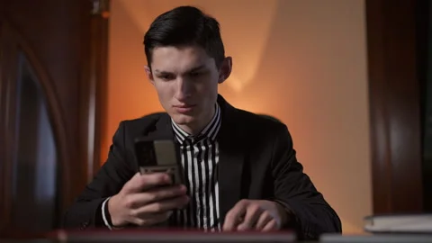 Young Man Dressed in a Sharp Suit is Intently Using a Mobile Phone While Seated Stock Footage 291542230
