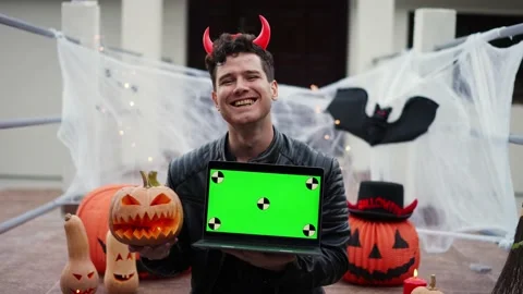 A young man dressed as a vampire devil with makeup holds a laptop with a green Stock Footage 219756619