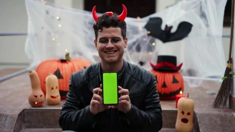A young man dressed as a vampire devil with makeup holds a phone with a green Vídeo Stock 219756670