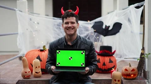 A young man dressed as a vampire devil with makeup holds a laptop with a green Stock Footage 250410178
