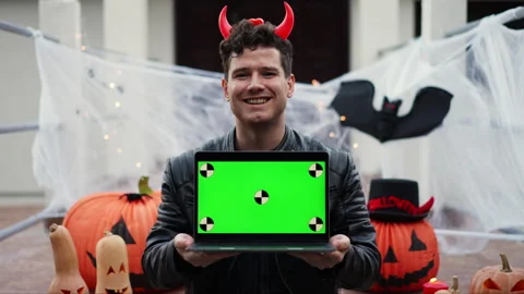 Young man dressed as a vampire devil with makeup holds a laptop with a green Stock Footage 289128559