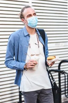 Young man dressing casual using surgical mask and holding in hands a coffee t Fotos de archivo