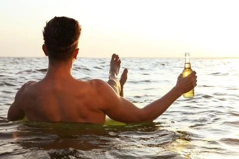 Young man with drink on inflatable ring in sea, back view Stock Photos