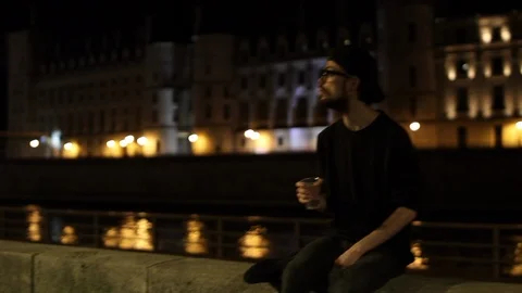 Young man drinking alone in the street next to the river docks in Paris by Stock Footage 92217669