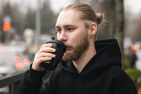 A young man drinking from a bamboo reusable cup outdoors. Stock Photos