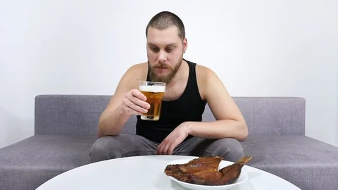 Young man drinking beer and eating dried fish sitting on the couch. Stock Footage 122755885