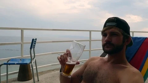 Young man drinking beer at beach during sunset Stock Footage 85027136