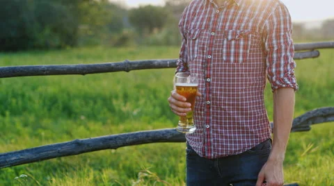 A young man drinking a beer on a hot day. He is wearing a hat in the countryside Stock Footage 65457346
