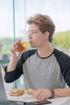 Young man drinking beer while eating a sandwich Stock Photos