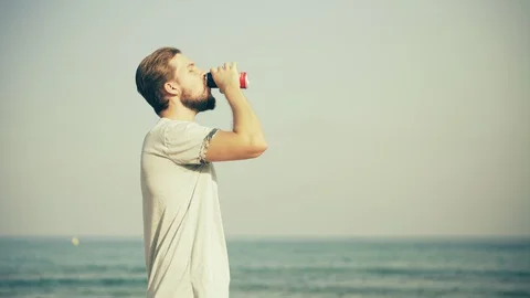 Young Man Drinking Beverage on Beach Stock Footage 129346222