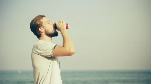 Young Man Drinking Beverage on Beach Stock Footage 129349641
