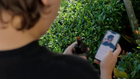 Young man drinking bottled coffee while scrolling smartphone outdoors... Stock Footage 323327838