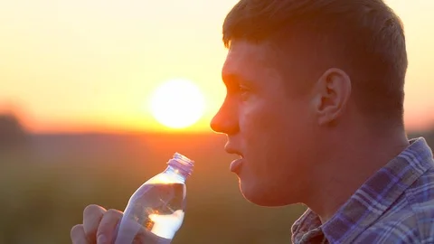 Young man drinking clear water from a plastic bottle in nature at wheat field Stock Footage 97014791