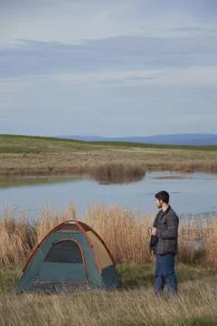 Young man drinking cofee next to a Tent Stock Photos
