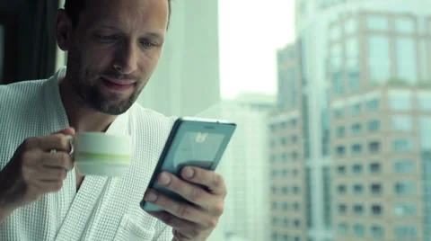 Young man drinking coffee and using smartphone by the window with the cityscape Stock Footage 38986587