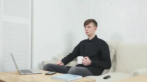 Young man drinking coffee and using laptop while talking on phone Stock Footage 73727318