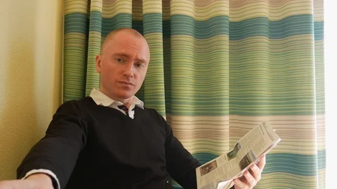 Young man drinking coffee and reading a newspaper in the hotel room. Travel Stock Footage 107106135