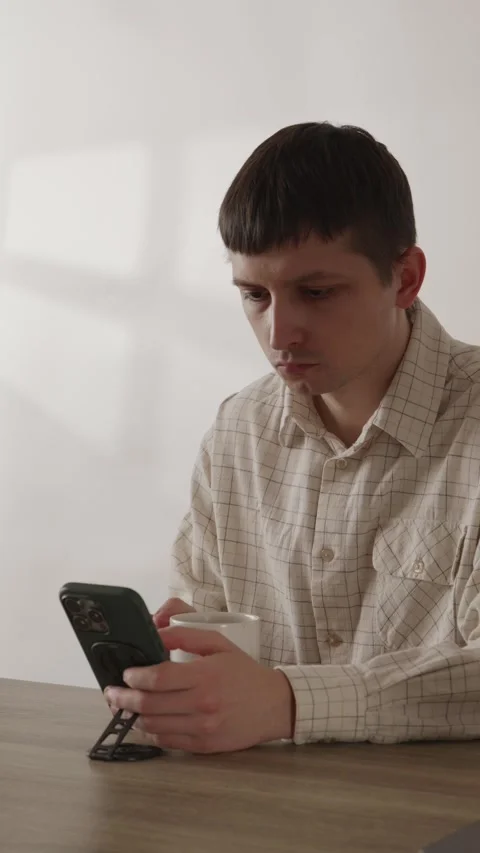 Young man drinking coffee and holding smartphone at wooden table Stock Footage 335082364