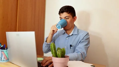 Young man drinking coffee from a blue cup in the office Stock Footage 292618247