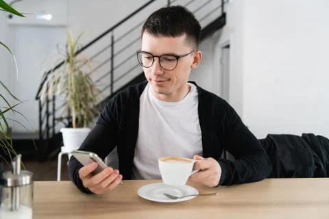 Young man drinking coffee in cafe and using phone Stock Photos