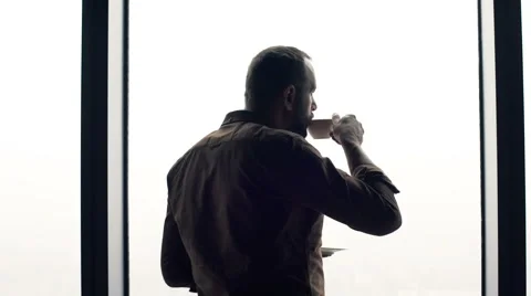 Young man drinking coffee close to the window at home Stock Footage 66765846