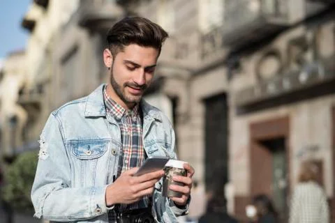 Young man drinking coffee to go and looking smartphone in the city Stock Photos
