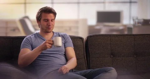Young man drinking coffee on his couch Video stock 78629388