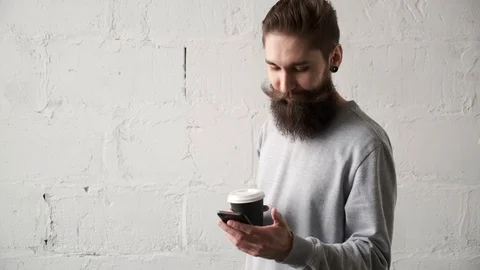 Young man drinking coffee, looking at  mobile phone . happy bearded guy smiling Video stock 124115061