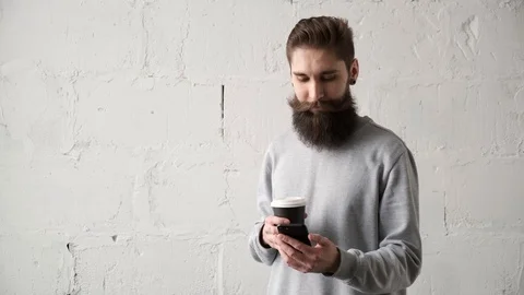 Young man drinking coffee, looking at  mobile phone . happy bearded guy smiling Stock Footage 124299855