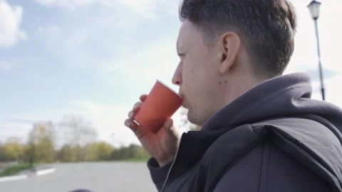 A young man drinking coffee while sitting on a park bench Stock Footage 253995792