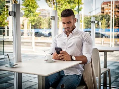 Young Man Drinking Coffee While Looking at Mobile Phone Foto stock