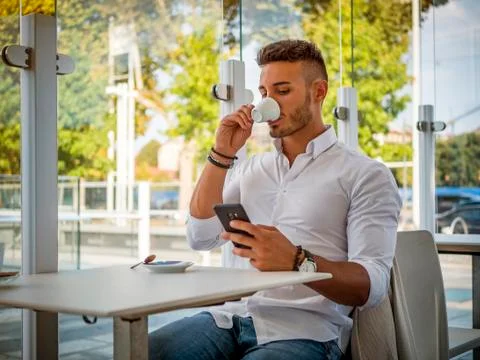 Young Man Drinking Coffee While Looking at Mobile Phone Stock Photos