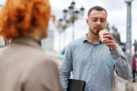 Young man drinking coffee while talking with a colleague on a city bridge Stock Photos