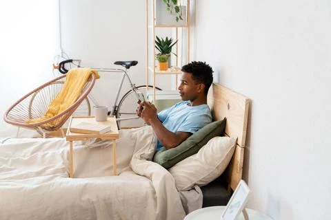 Young man drinking a cup of coffee and using a telephone in bed. Stock Photos