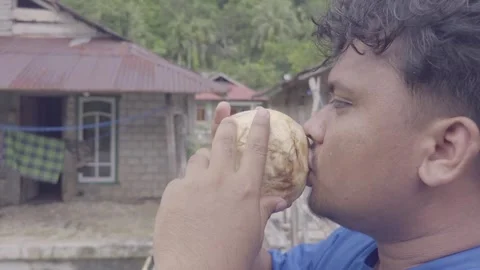 Young man drinking fresh coconut water in tropical village no audio Vídeos de archivo 332589973