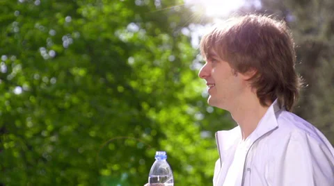 Young man drinking fresh water from the bottle in the sunny park Vidéo 39080334