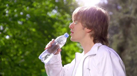 Young man drinking fresh water from the bottle in the sunny park 動画素材 39090015