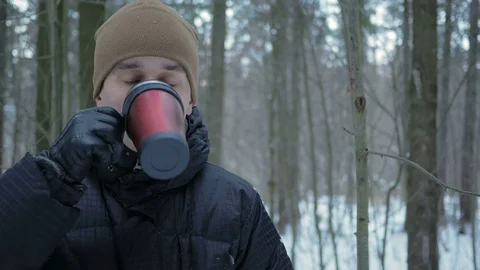 A young man drinking a hot beverage from a thermos in a winter forest. The man Stock Footage 71213069