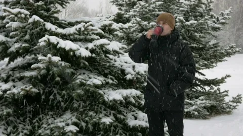 A young man drinking a hot beverage from a thermos in a winter forest. Big Stock Footage 71214013
