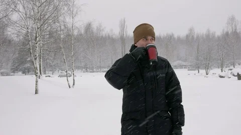 A young man drinking a hot beverage from a thermos in a winter forest. Big Stock Footage 71218397