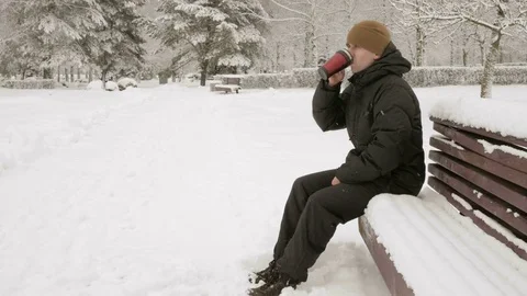 A young man drinking a hot beverage from a thermos in a winter park. Big Stock Footage 71222235